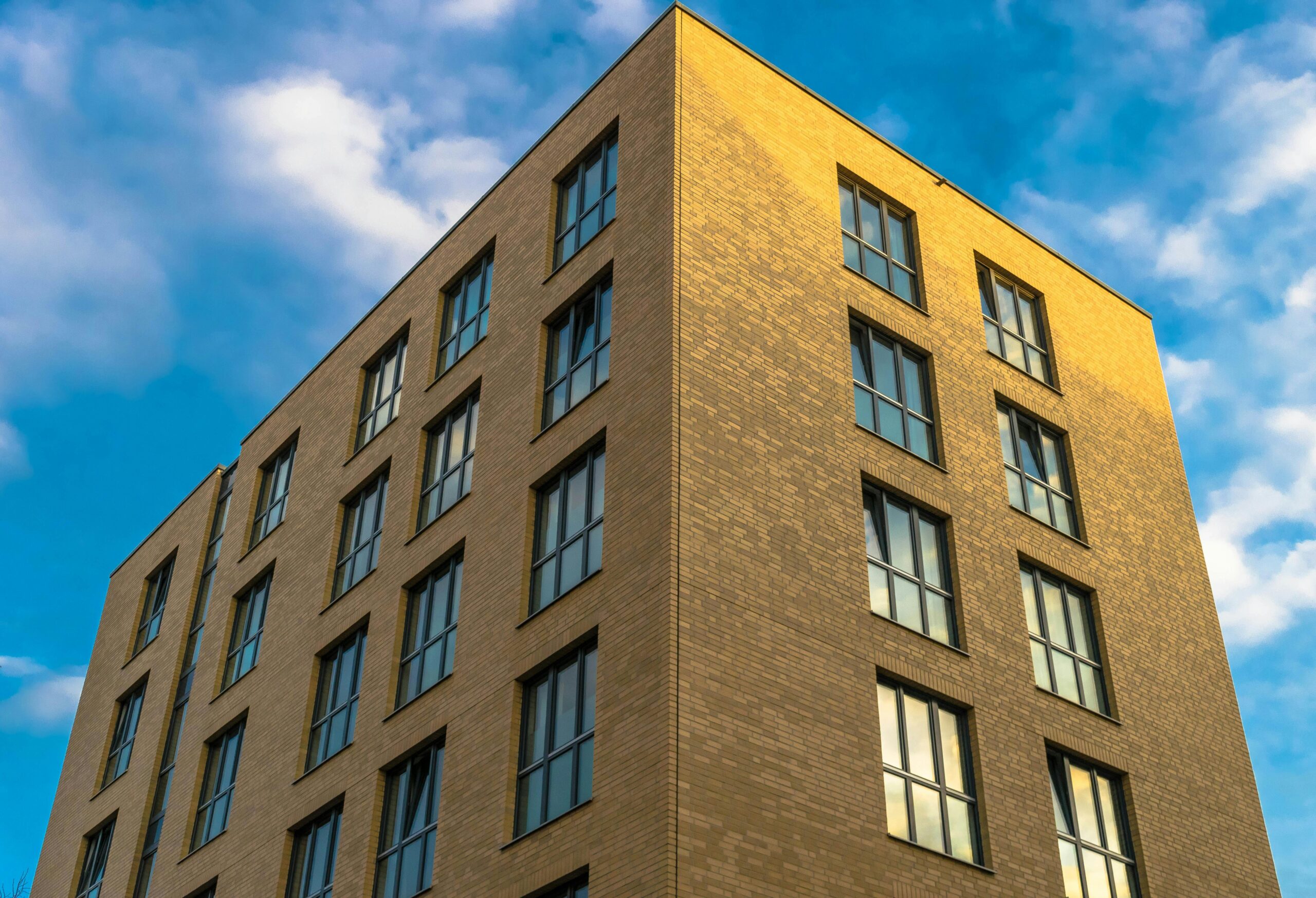 Low angle view of a modern brick building with clouds in the blue sky.